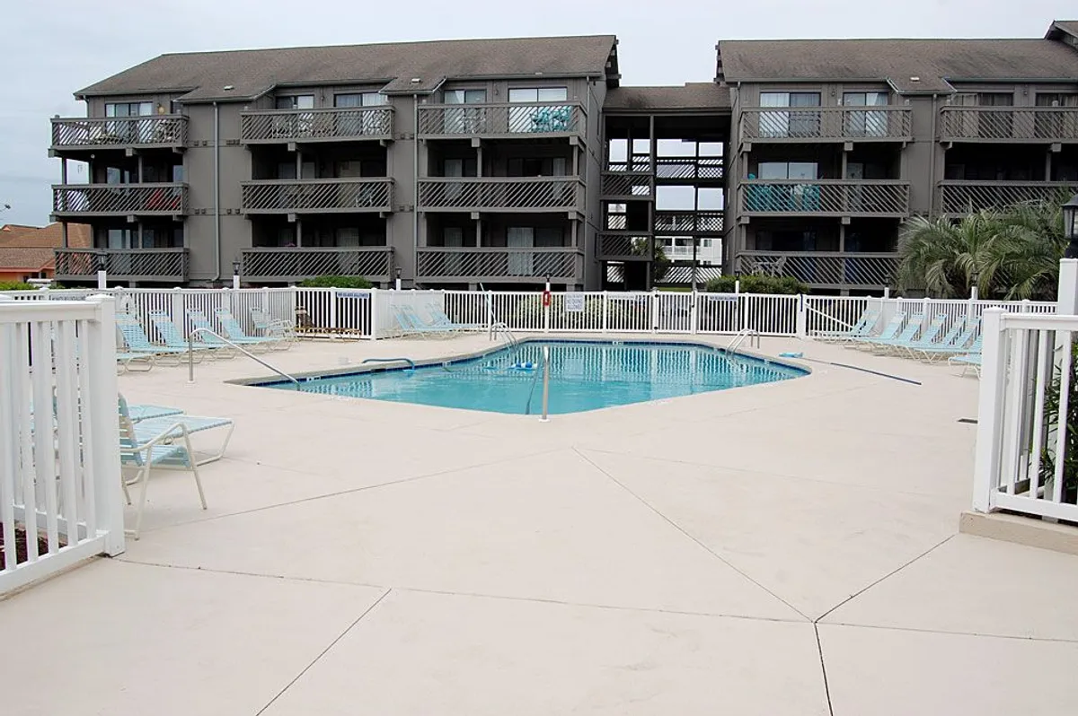 This image shows a vibrant swimming pool surrounded by lounge chairs and the building’s balconies, suggesting a lively resort atmosphere. Groups of people can gather for swimming, sunbathing, or casual chats. The wide angle captures both pools and balconies, highlighting the social aspect of the amenities.