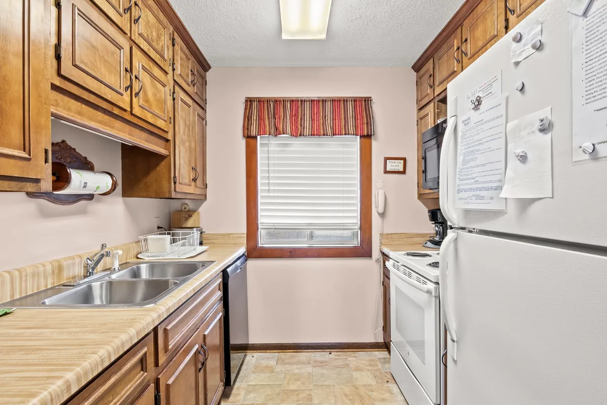 A cozy kitchen scene featuring a sink, countertop, window, fridge, and stove. The space invites cooking, baking, and gathering, evoking the comforts of home and flexibility for families or groups.