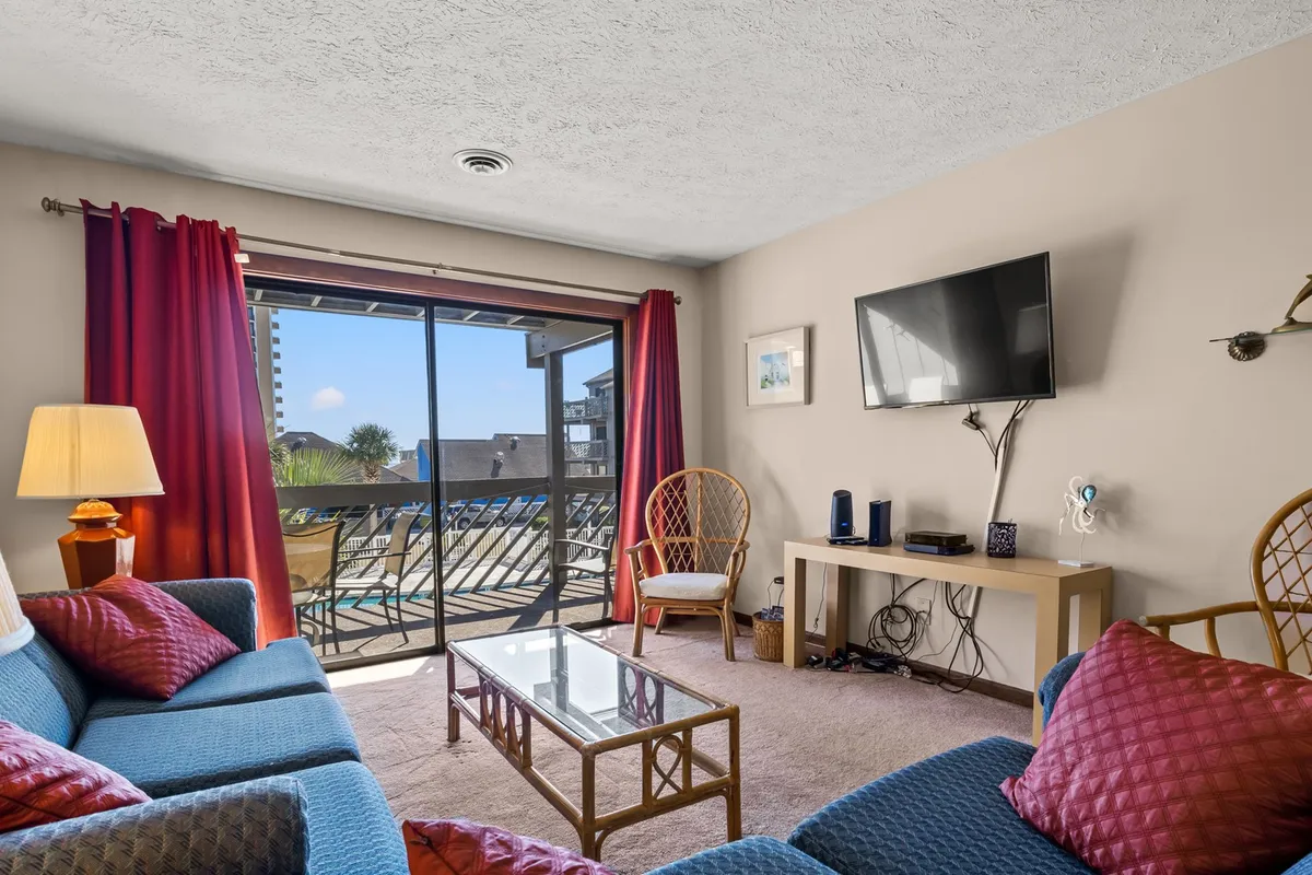 A cozy living room featuring a plush sofa, large window with red curtains, a coffee table, and a TV. Sunlight streams in, creating an inviting atmosphere suitable for relaxing, watching movies, and enjoying time together.