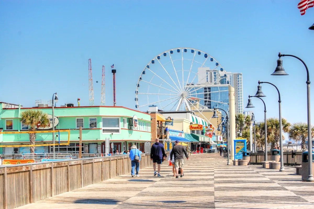 This dynamic exterior image captures the iconic Myrtle Beach Ferris wheel, flanked by colorful buildings, a lively boardwalk, and swaying palm trees. It radiates an atmosphere of fun and excitement, encouraging exploration and enjoyment of local attractions.