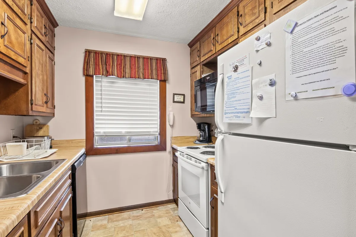 A bright, fully equipped kitchen with modern appliances, window with blinds, wooden cabinetry, and a kitchen sink. The space is designed for meal preparation and group participation, fulfilling both function and warmth.